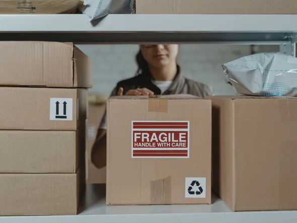 A person organizing fragile cardboard boxes in a warehouse setting.