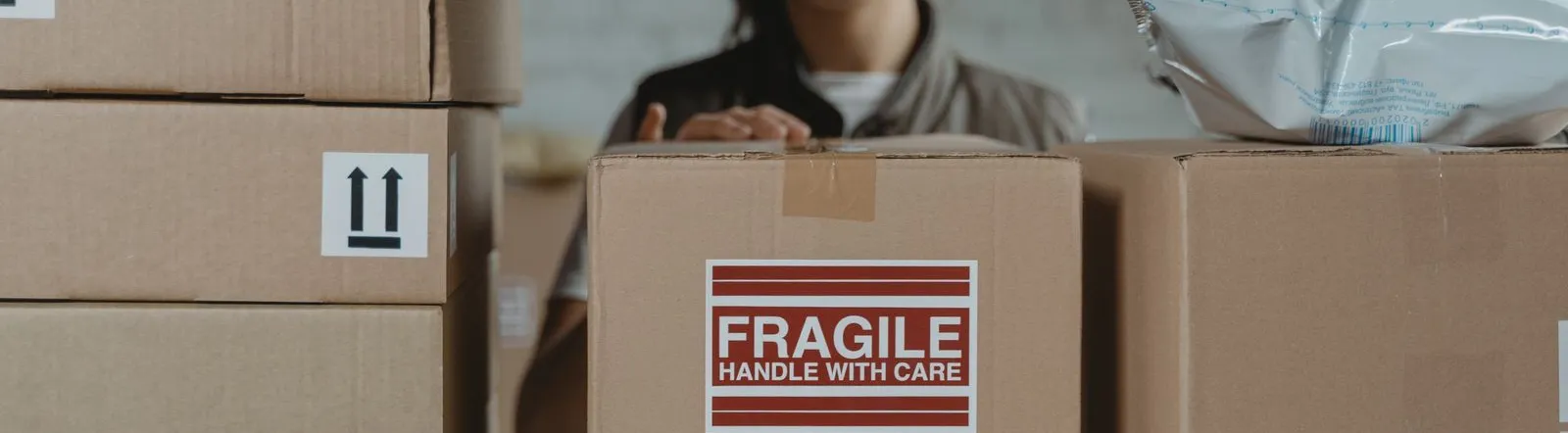 A person organizing fragile cardboard boxes in a warehouse setting.
