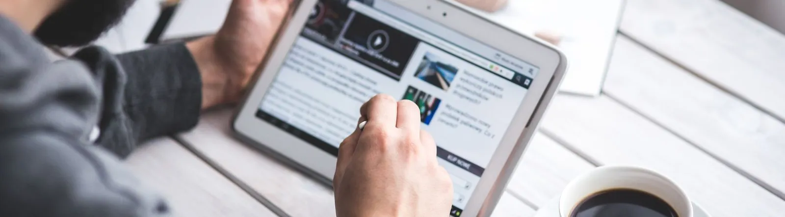 A man uses a tablet to browse news while enjoying a cup of coffee, stylus in hand.