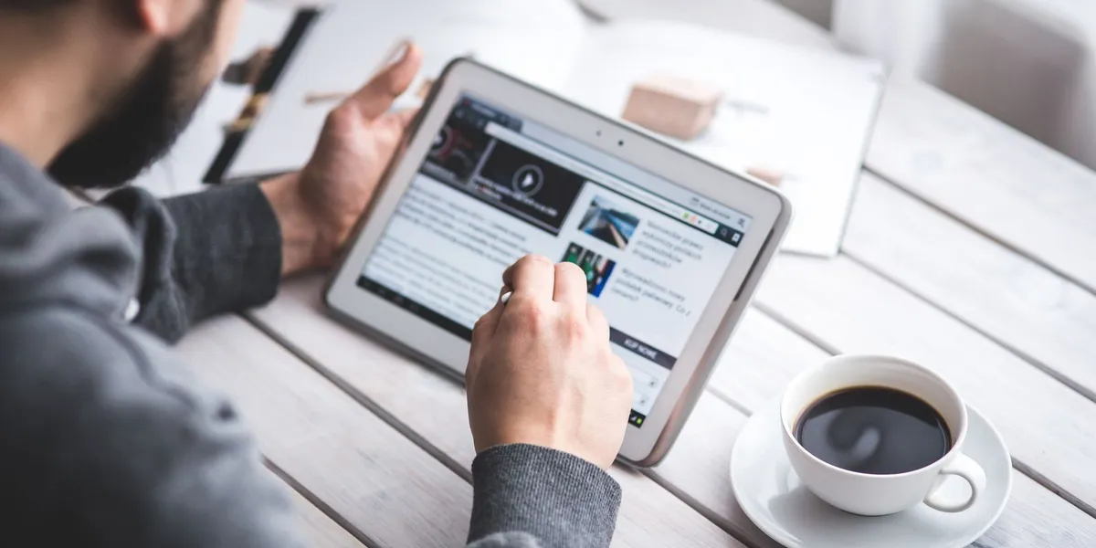 A man uses a tablet to browse news while enjoying a cup of coffee, stylus in hand.