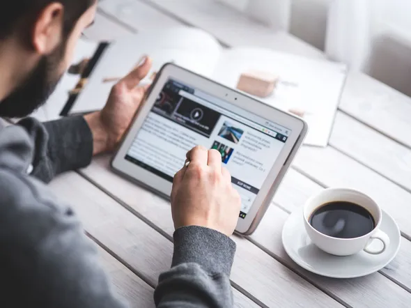 A man uses a tablet to browse news while enjoying a cup of coffee, stylus in hand.