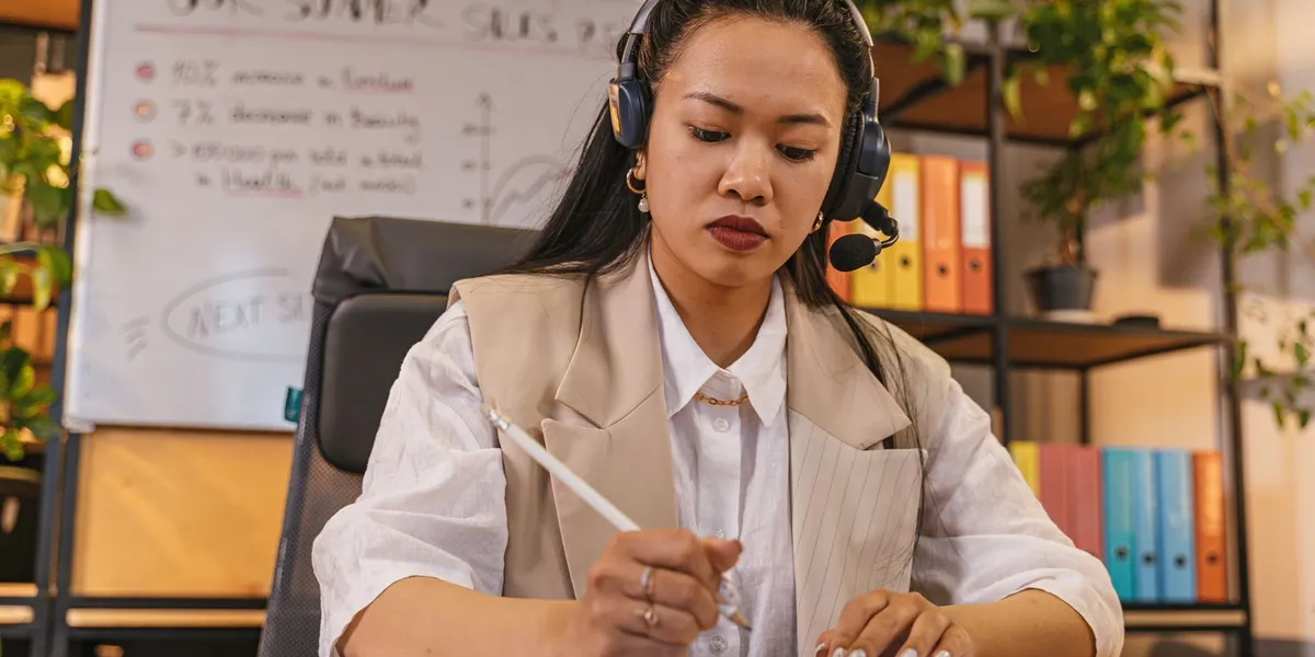 Professional woman wearing a headset taking notes in an office setting, focused on work.