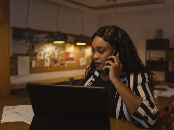 African American woman in a striped blazer making a phone call in a modern office.