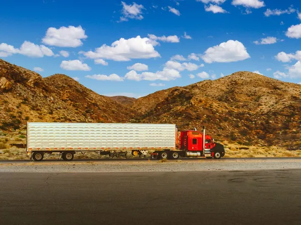 A vibrant red semi-truck travels through a desert highway with mountain views in Nevada.