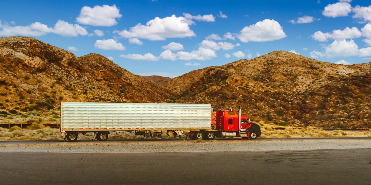 A vibrant red semi-truck travels through a desert highway with mountain views in Nevada.