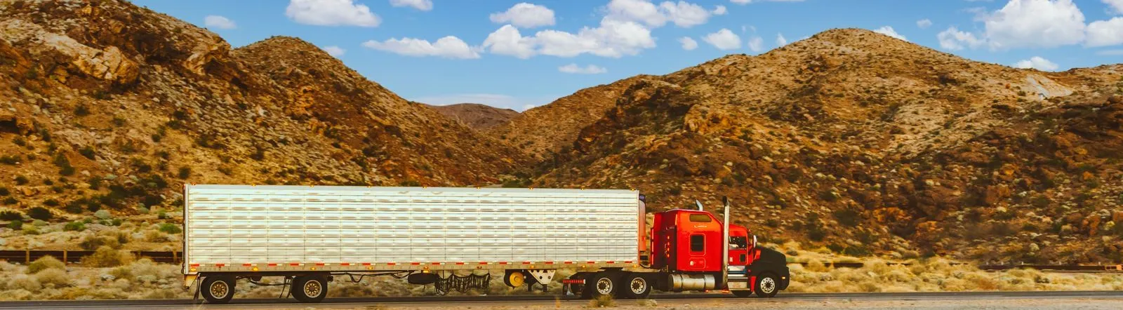 A vibrant red semi-truck travels through a desert highway with mountain views in Nevada.
