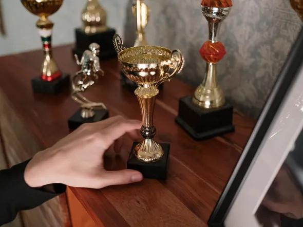 A close-up of a hand reaching for a shiny trophy on a wooden shelf, symbolizing success.