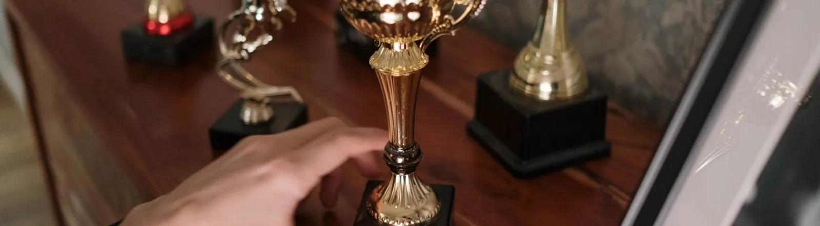 A close-up of a hand reaching for a shiny trophy on a wooden shelf, symbolizing success.