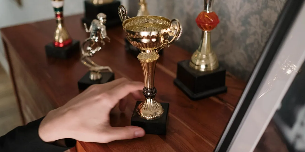A close-up of a hand reaching for a shiny trophy on a wooden shelf, symbolizing success.