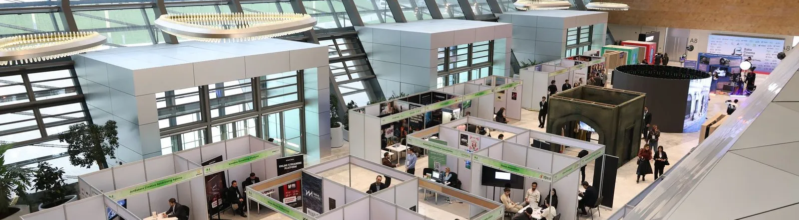 A bustling trade show exhibition inside a modern hall with people networking and exploring booths.