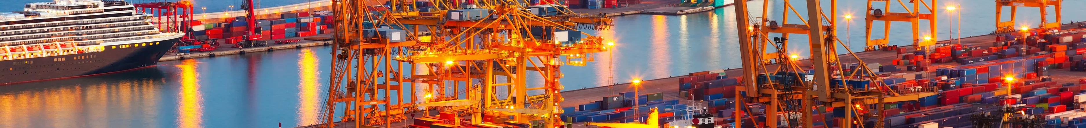 Night view of an active commercial port with lit cranes and docked cargo ships