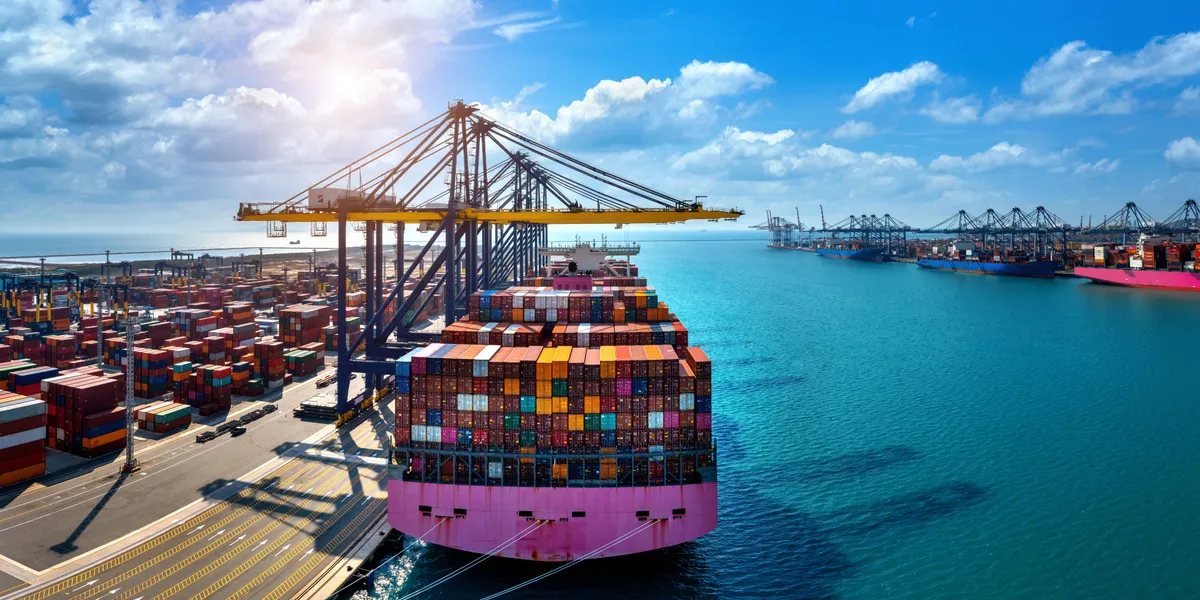 Aerial view of a loaded container ship arriving at a busy port with stacked cargo