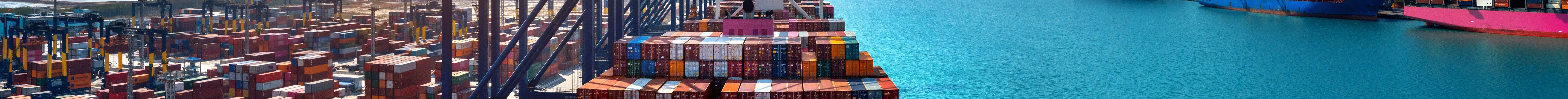 Aerial view of a loaded container ship arriving at a busy port with stacked cargo