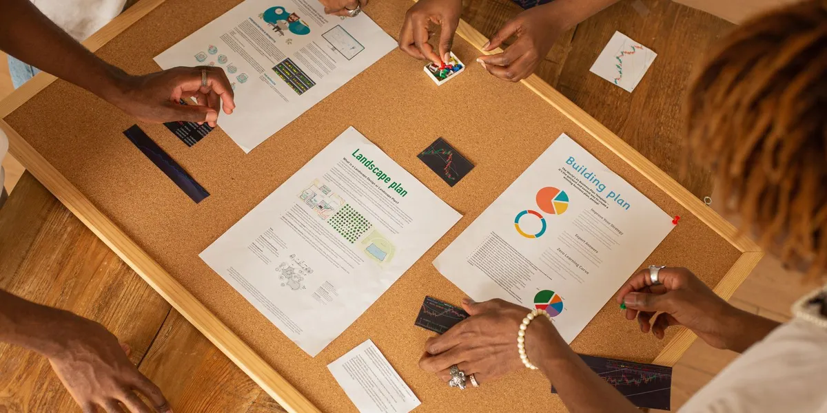 A diverse team collaborates on a workspace board with charts and plans.