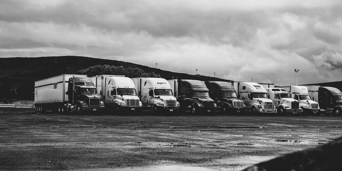 Row of parked semi trucks in a rainy lot, captured in a dramatic black and white setting.