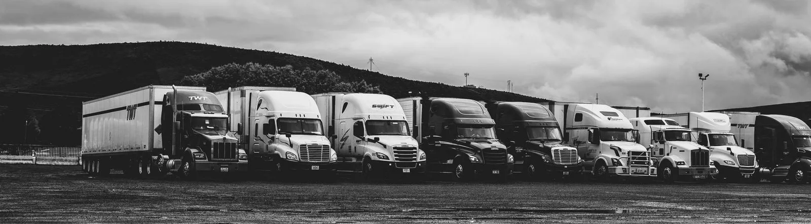 Row of parked semi trucks in a rainy lot, captured in a dramatic black and white setting.