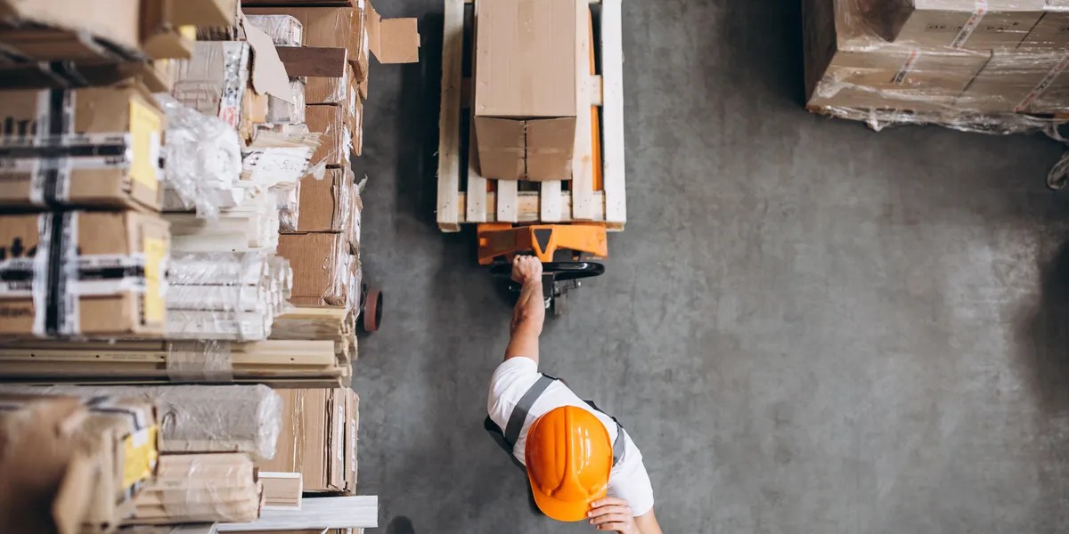 Worker with hard hat pulling a loaded pallet truck through a warehouse