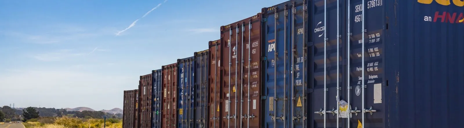 Colorful cargo containers on a freight train along a rural railway track under a clear blue sky.