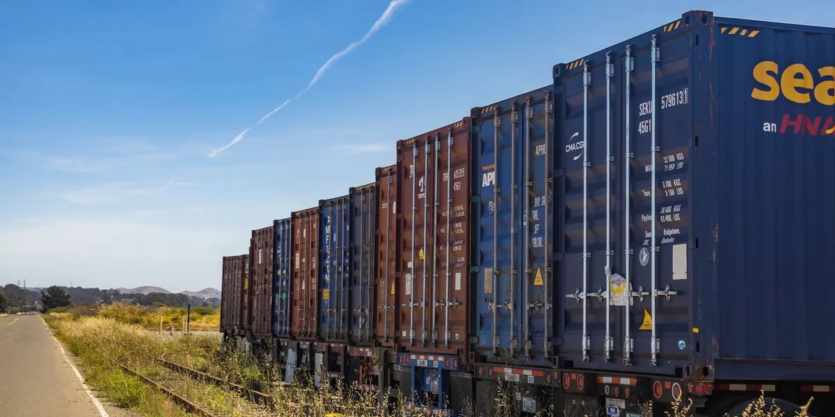 Colorful cargo containers on a freight train along a rural railway track under a clear blue sky.