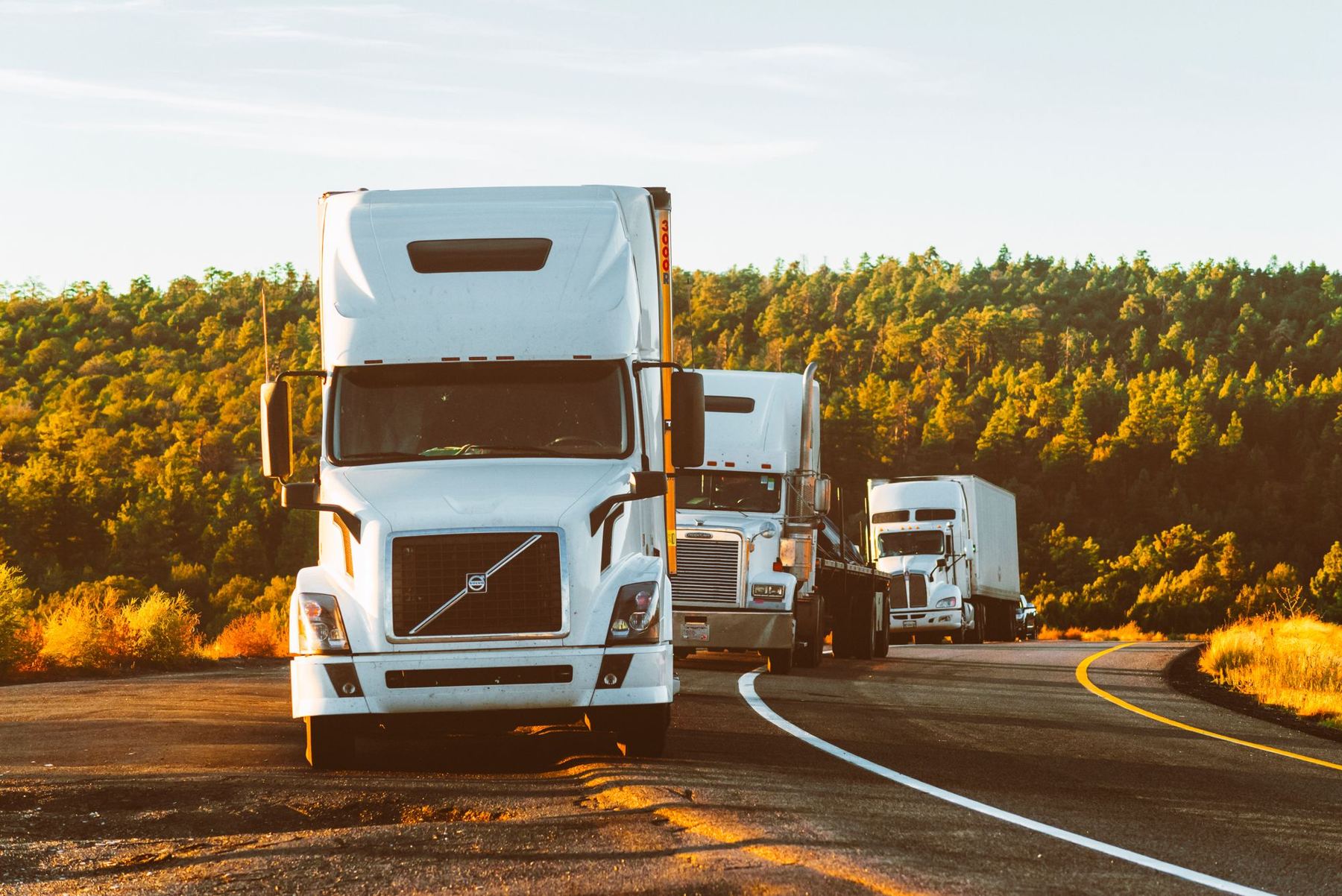 Three semi-trucks on a highway at sunset