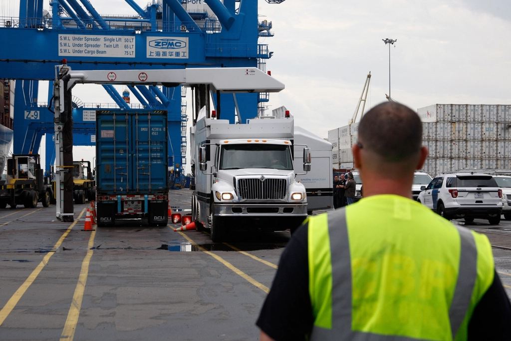 Officer in a high-visibility vest watching a truck at a port gate